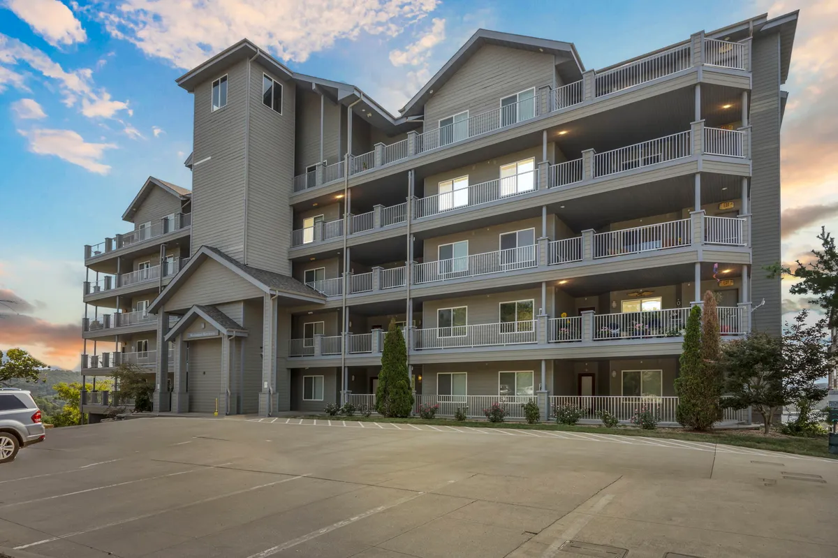 A modern multi-level building with inviting balconies and a landscaped area in front. People are seen walking, socializing, and enjoying the view, suggesting a lively and welcoming atmosphere. The exterior hints at the upscale accommodations and ease of access to outdoor activities.