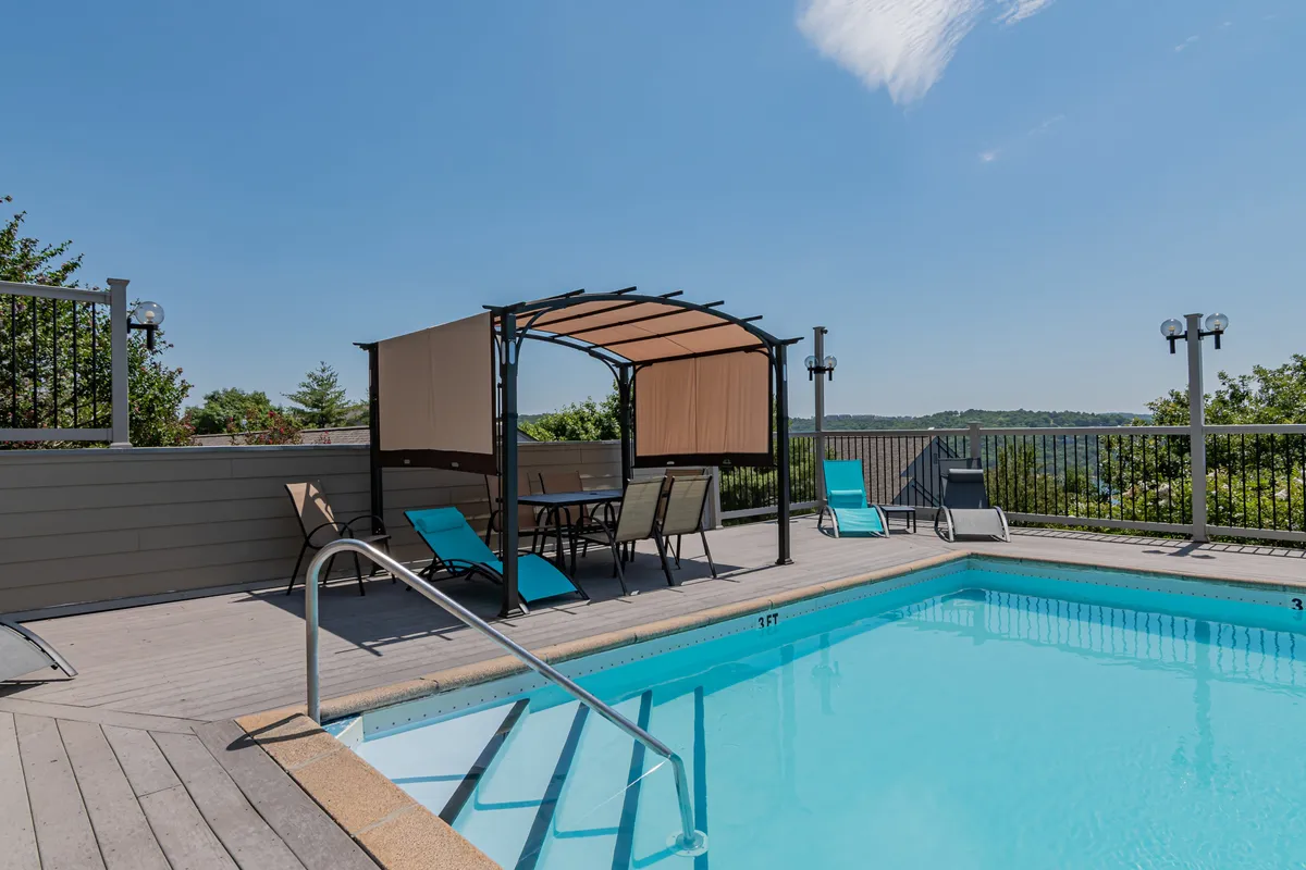 A stylish outdoor swimming pool area surrounded by lounge chairs and a canopy seating area. The view extends to a landscaped backdrop, showcasing a tranquil, resort-like environment ideal for relaxation, social gatherings, and swimming.