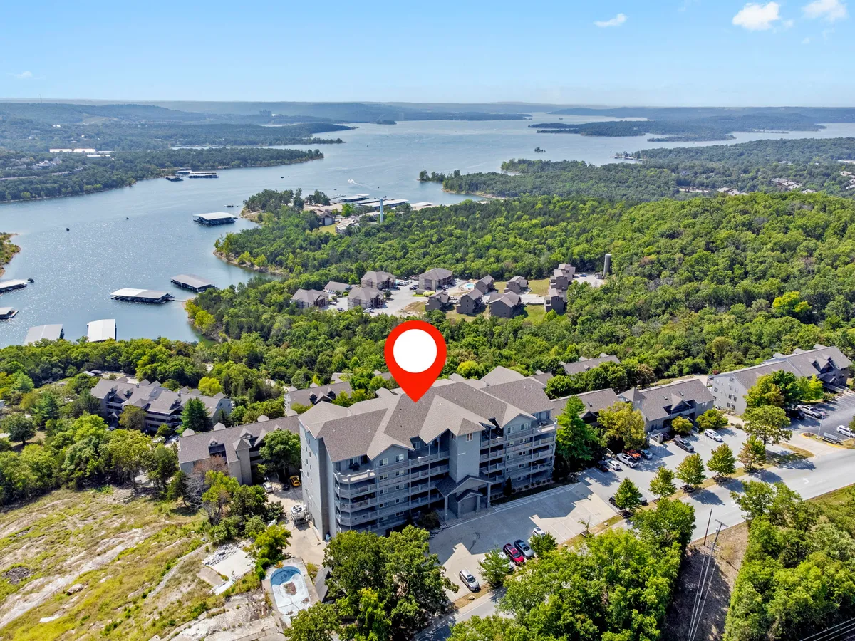 A scenic exterior shot featuring Table Rock Lake bordered by lush greenery, with a building and parking lot in the foreground. The scene is tranquil, and the lake is perfect for boating and lakeside picnics, while the surrounding area suggests nearby nature trails and opportunities for exploration.