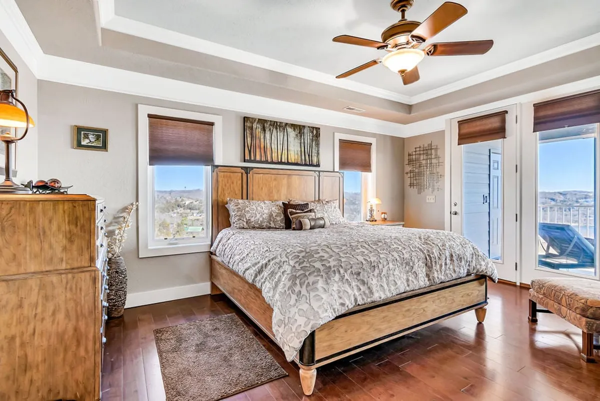 A serene king bedroom featuring a large, comfortable bed with stylish bedding, decorative wall art, a dresser, and expansive windows that flood the room with natural light. The decor is soothing and contemporary, creating a restful environment ideal for relaxation.