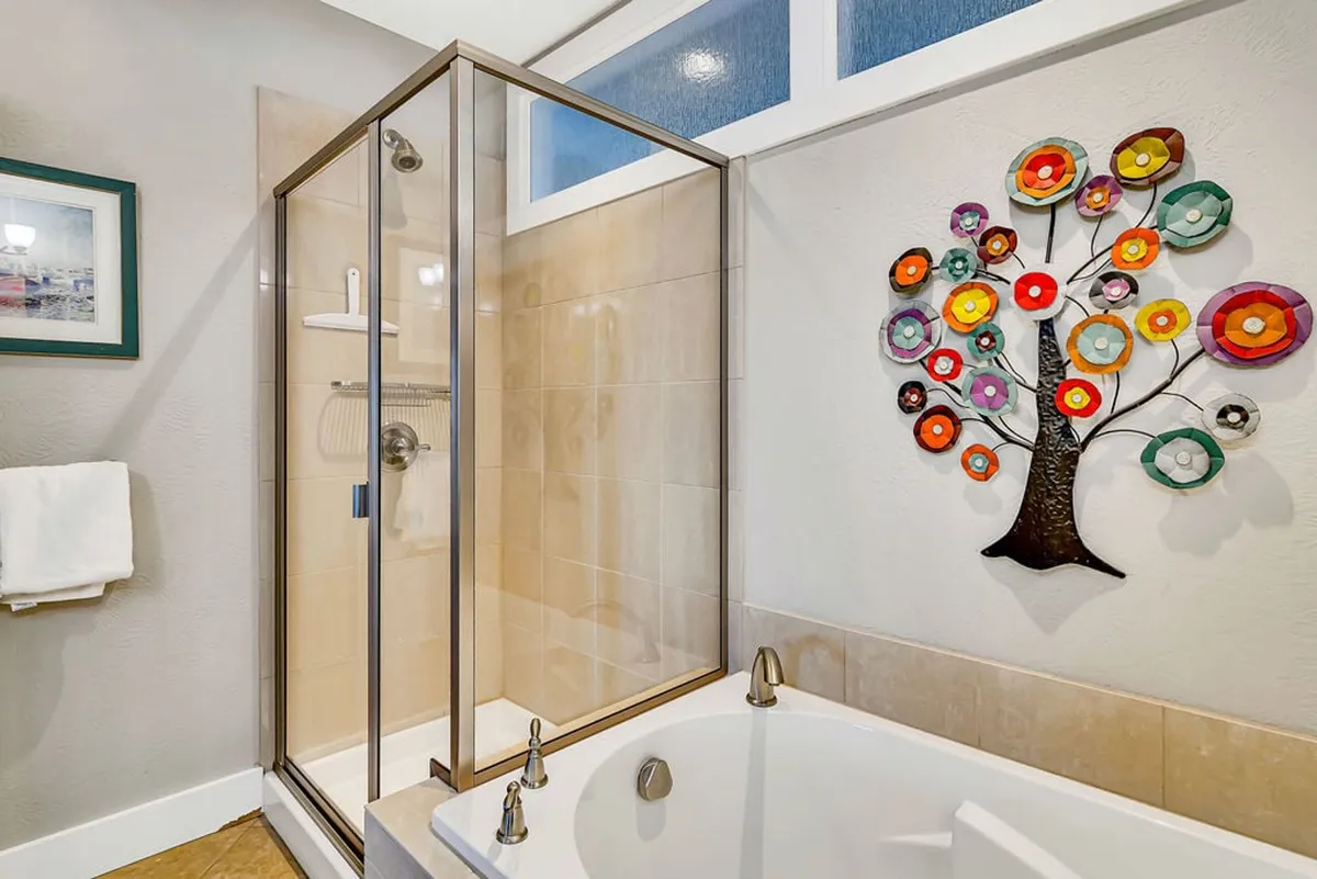 A luxurious bathroom with a glass shower enclosure, a soaking bathtub, and colorful decorative tree art that adds personality and vibrancy to the space. The mood is serene and rejuvenating, ideal for unwinding after a day by the lake.