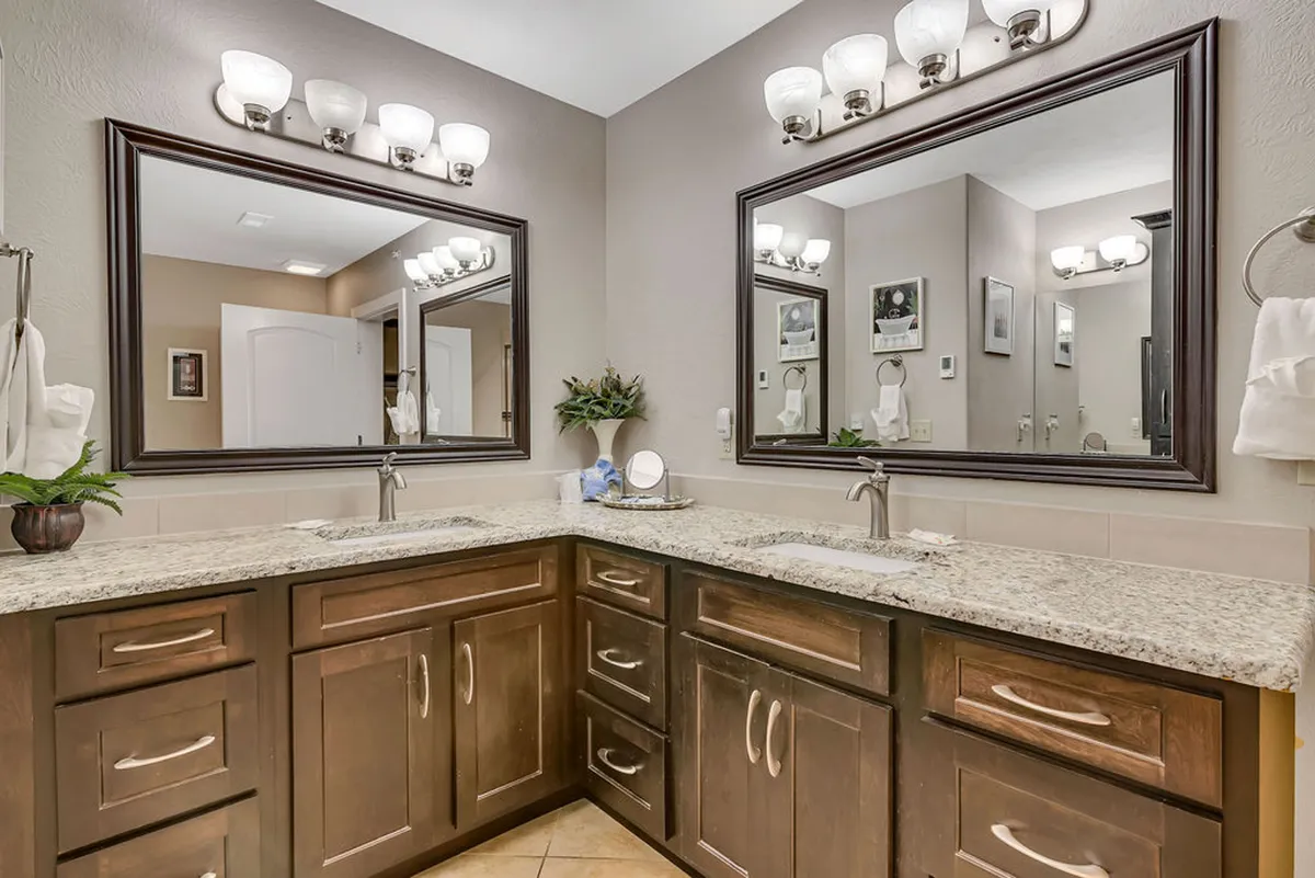 A modern bathroom featuring double sinks set in a granite countertop, large mirrors, and elegant lighting fixtures. The overall mood is spa-like, inviting, and perfect for morning and evening routines.