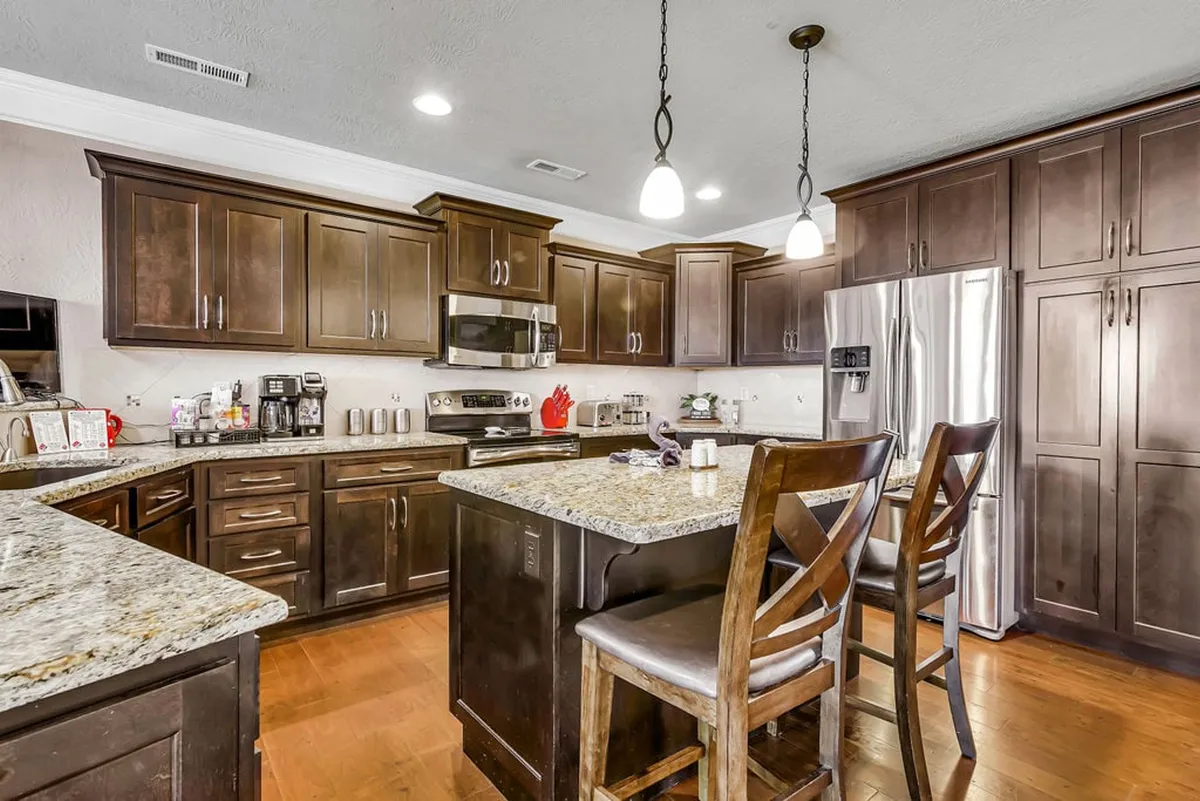 A modern kitchen highlighted by sleek granite countertops, rich dark wood cabinets, and stainless steel appliances. Bar stools at the counter invite guests to participate in meal prep or enjoy casual snacks, while the layout supports both cooking and entertaining.
