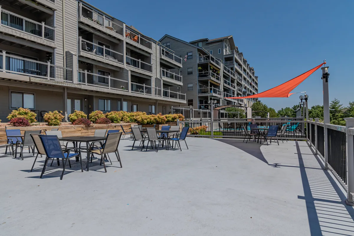 A cheerful outdoor seating area surrounded by colorful flowers, a sunshade, and attractive building architecture. The space feels inviting and is perfect for family gatherings, morning coffee, or relaxing after a day of adventure.