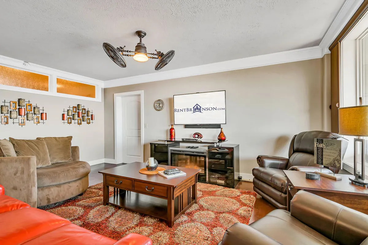 The image shows a stylish, inviting living room with a plush sofa, contemporary coffee table, a large TV, and tasteful wall art. The space is bathed in natural light, arranged for both relaxing movie nights and cozy conversations, creating an atmosphere perfect for gathering with friends or family.