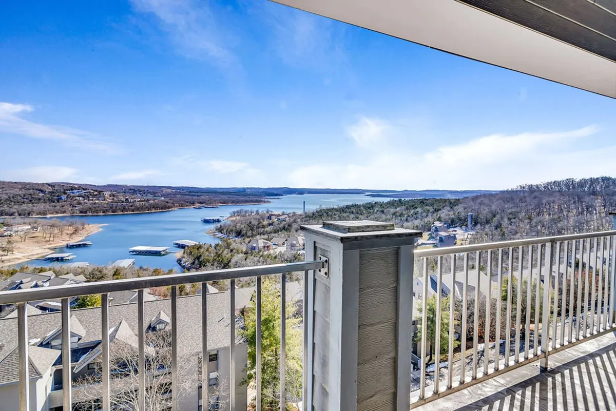 A panoramic lakeview from a balcony, with the lake stretching out to the horizon under a wide sky. The balcony railing invites guests to imagine themselves relaxing, enjoying the water view, and watching boats glide across the shimmering surface.