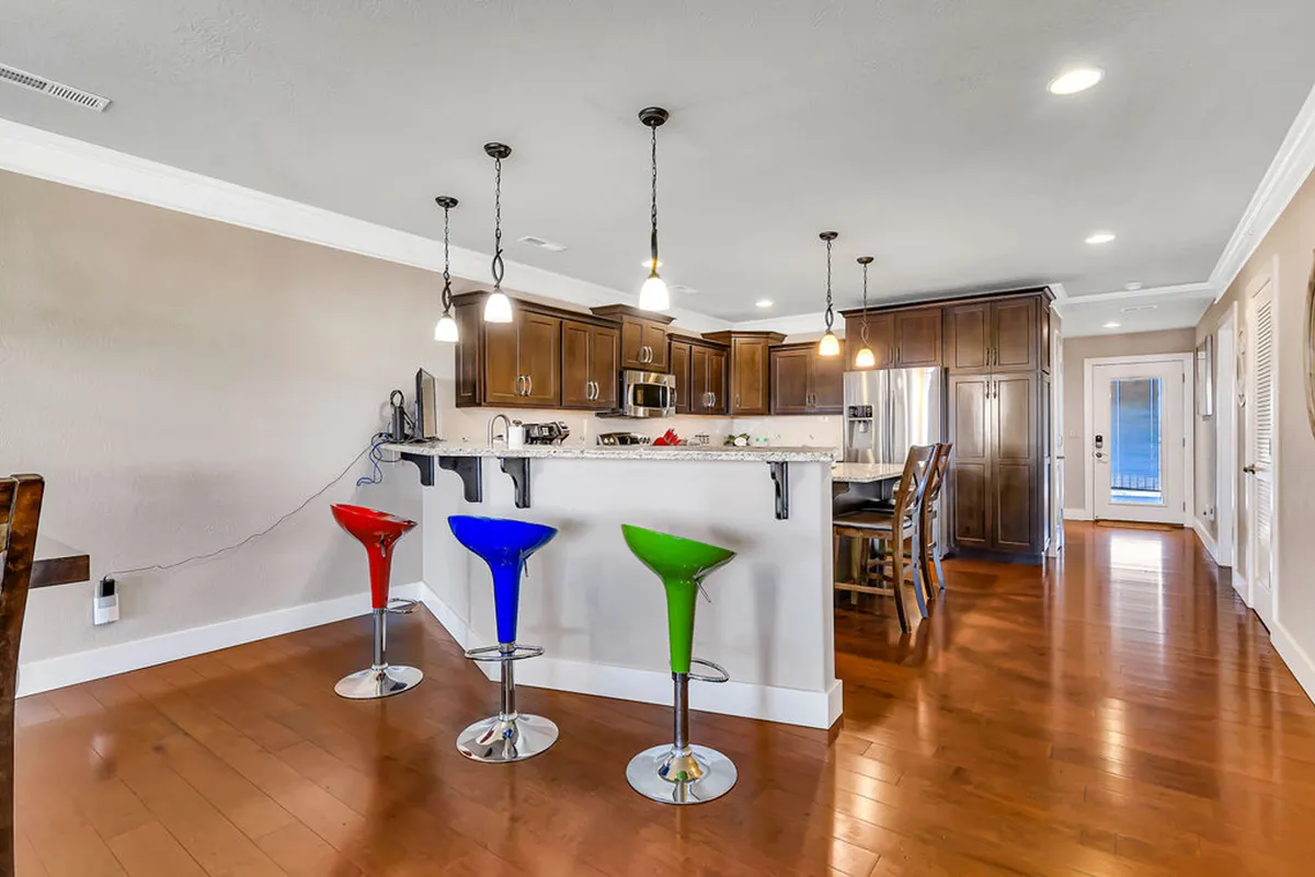 A stylish and modern kitchen interior featuring colorful bar stools, a spacious kitchen island, and sleek cabinetry. The atmosphere is lively—ideal for casual dining, entertaining, or preparing drinks before heading out for the evening.