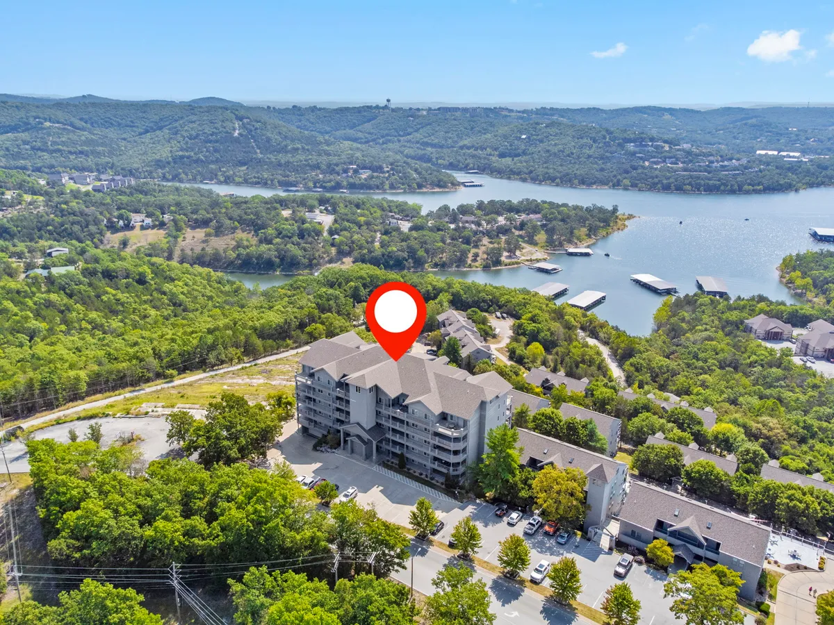 A sweeping exterior view of the main building, surrounded by greenery, with Table Rock Lake and distant hills in the background. The image captures the proximity of the resort to the lake and highlights the area's natural beauty.